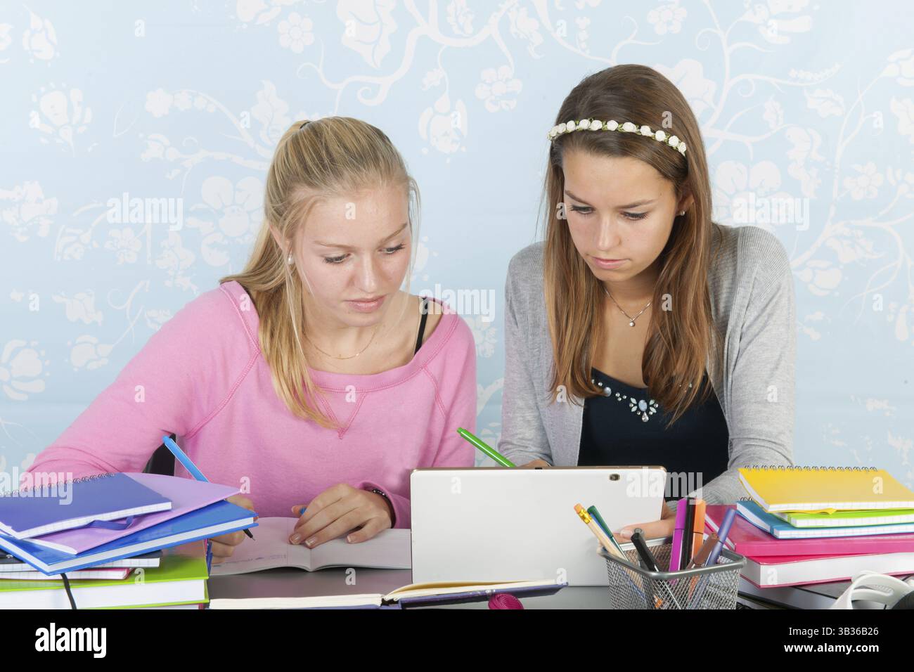 Two teengirls sitting at desk making homework together using a digital tablet Stock Photo