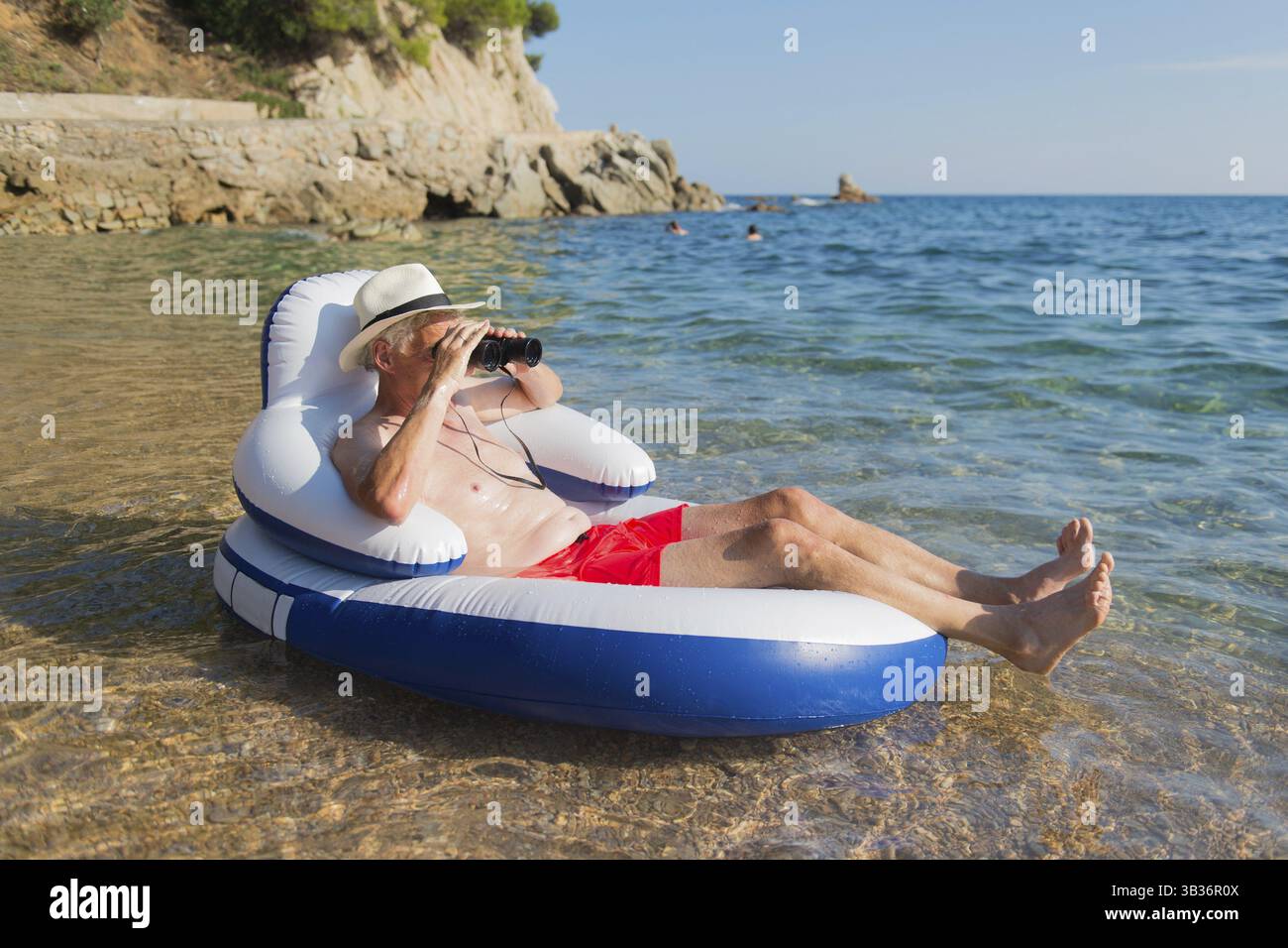 Senior man with spy glasses floating on chair in the sea Stock Photo