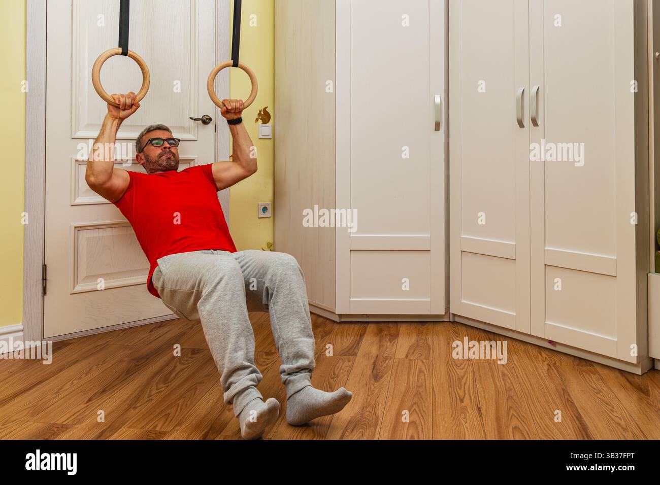 A man performs a rowing exercise using gymnastic rings indoors. He is ...