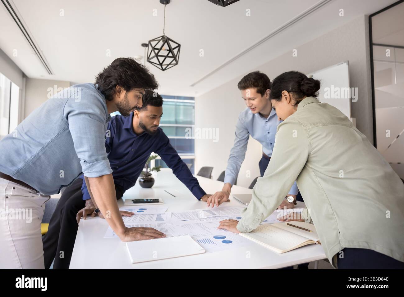 Team reviewing financial reports, analyzing revenue gathered around conference table Stock Photo