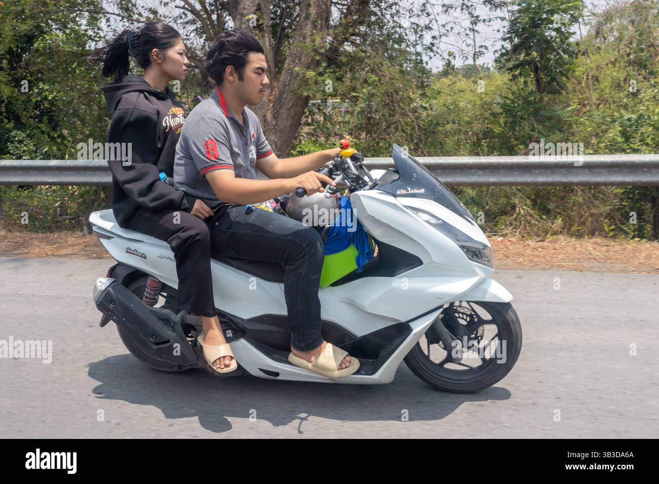 THAILAND, APR 15 2024, A couple is riding a motorcycle along the side of the highway Stock Photo