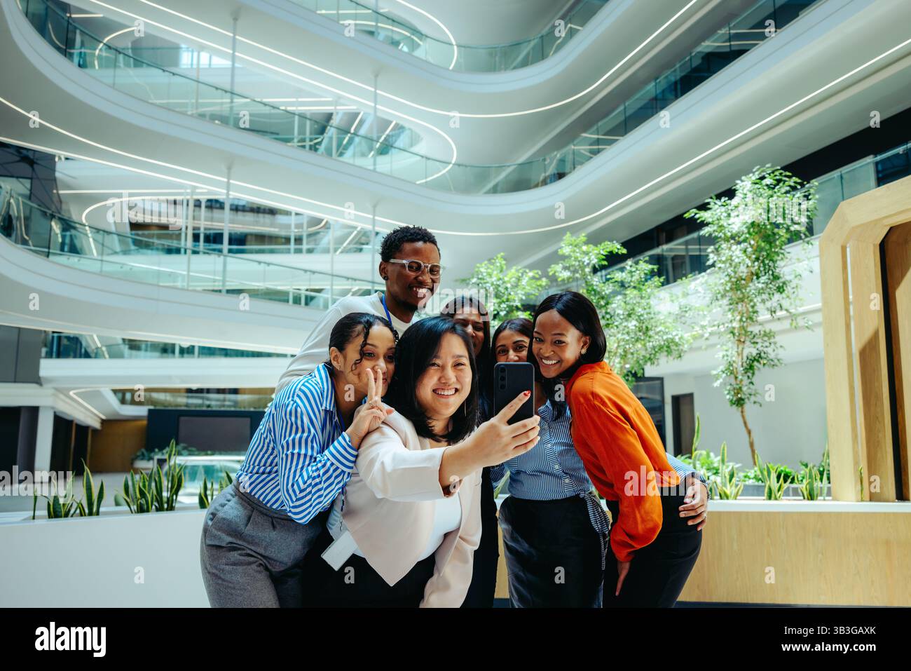 A cheerful group of colleagues gathers to take a selfie in a modern ...