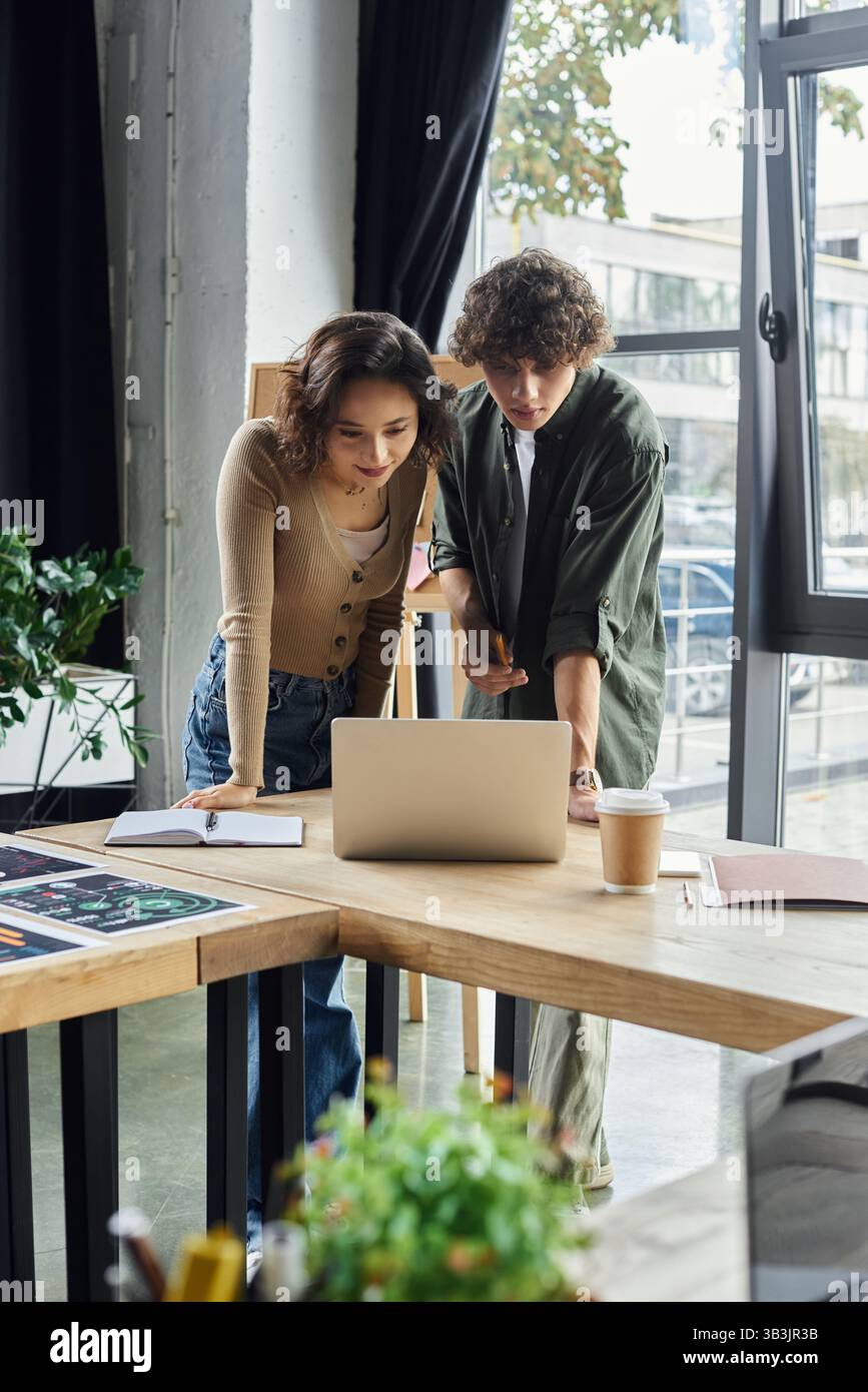 Two colleagues engage in a focused discussion while reviewing digital content at their workspace. Stock Photo
