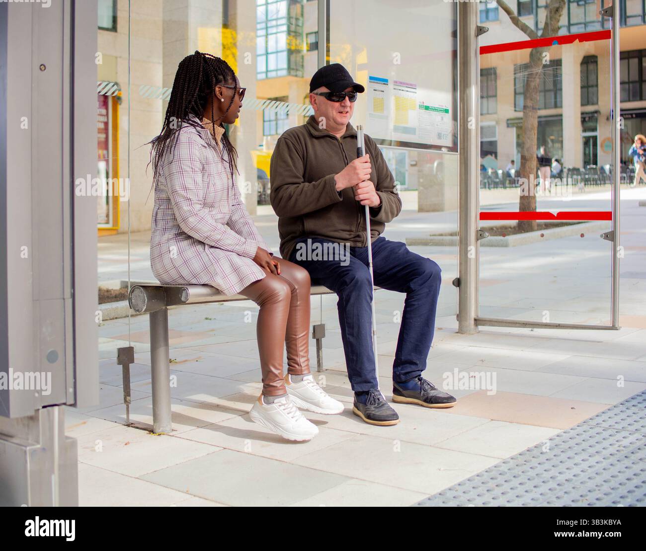 Blind man with a guide cane speaks with a woman at the bus stop. Stock Photo
