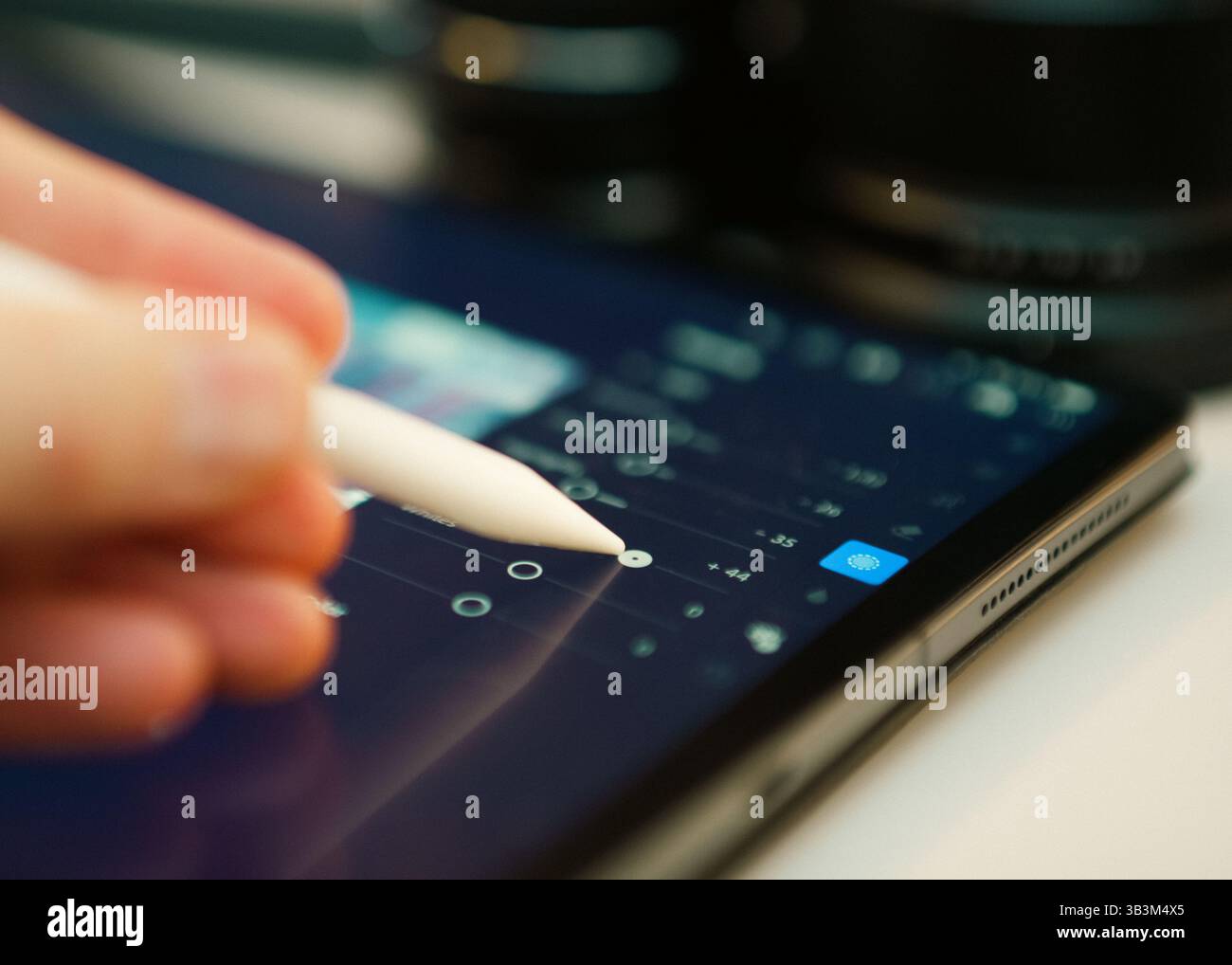 Close-up person using digital stylus tablet screen adjust image parameters photo editing software, likely Lightroom. Interface shows sliders editing e Stock Photo