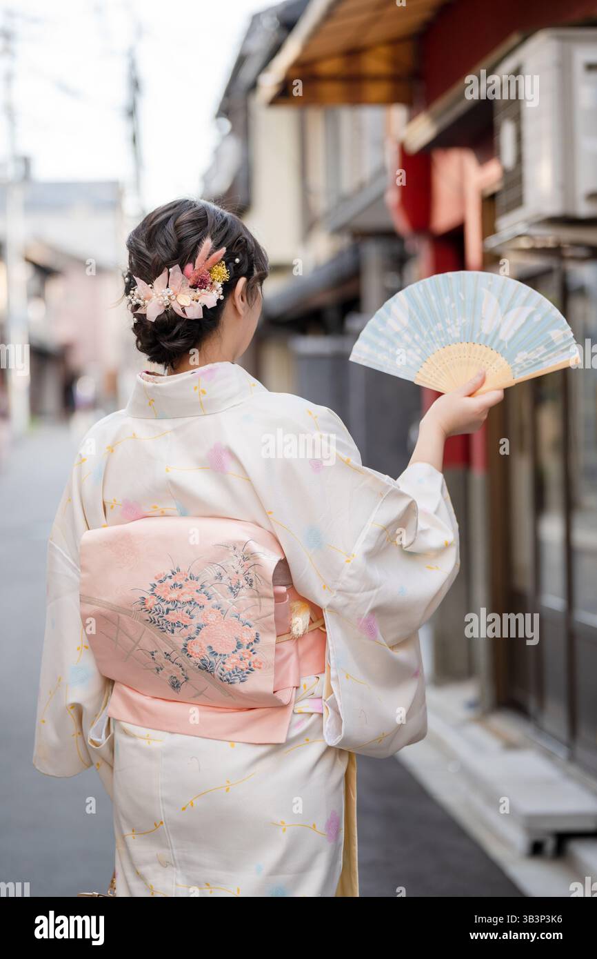 Woman in traditional Kimono holding a folding fan walks along a historic street in Kyoto, Japan Stock Photo