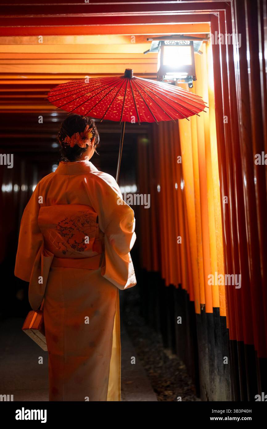 Woman in Kimono with red umbrella walking through the iconic red Torii ...