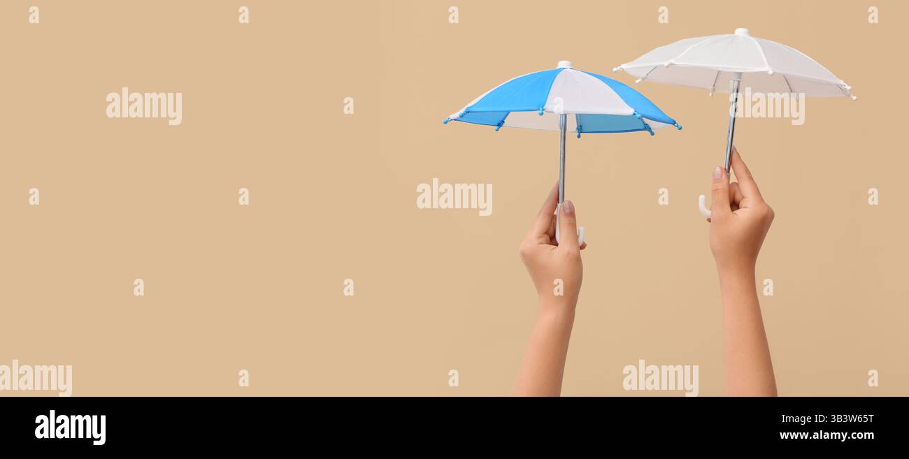 Hands holding small umbrellas on beige background with space for text Stock Photo