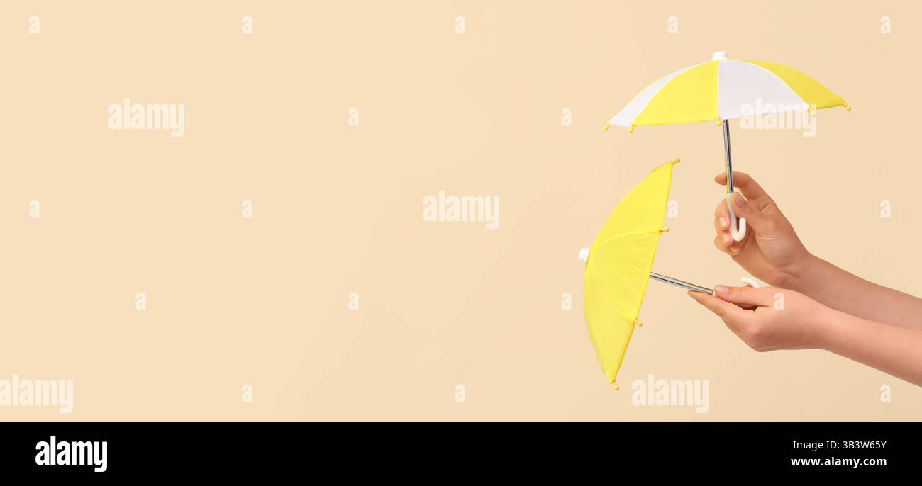 Hands holding small umbrellas on beige background with space for text Stock Photo