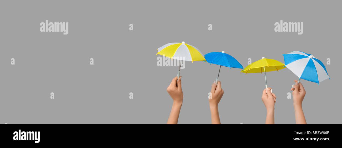 Hands holding small umbrellas on grey background with space for text Stock Photo