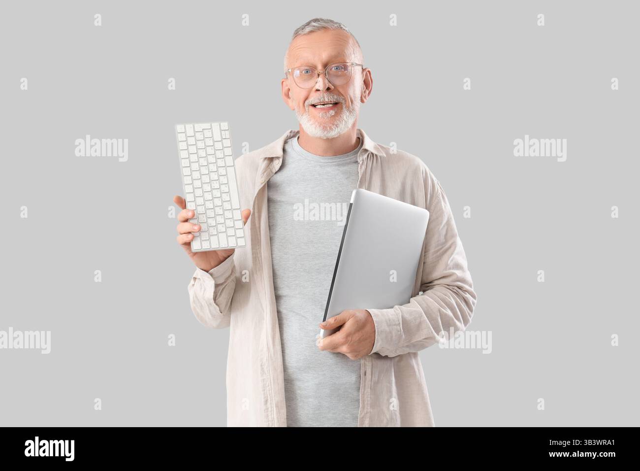 Mature programmer with laptop and computer keyboard on light background Stock Photo