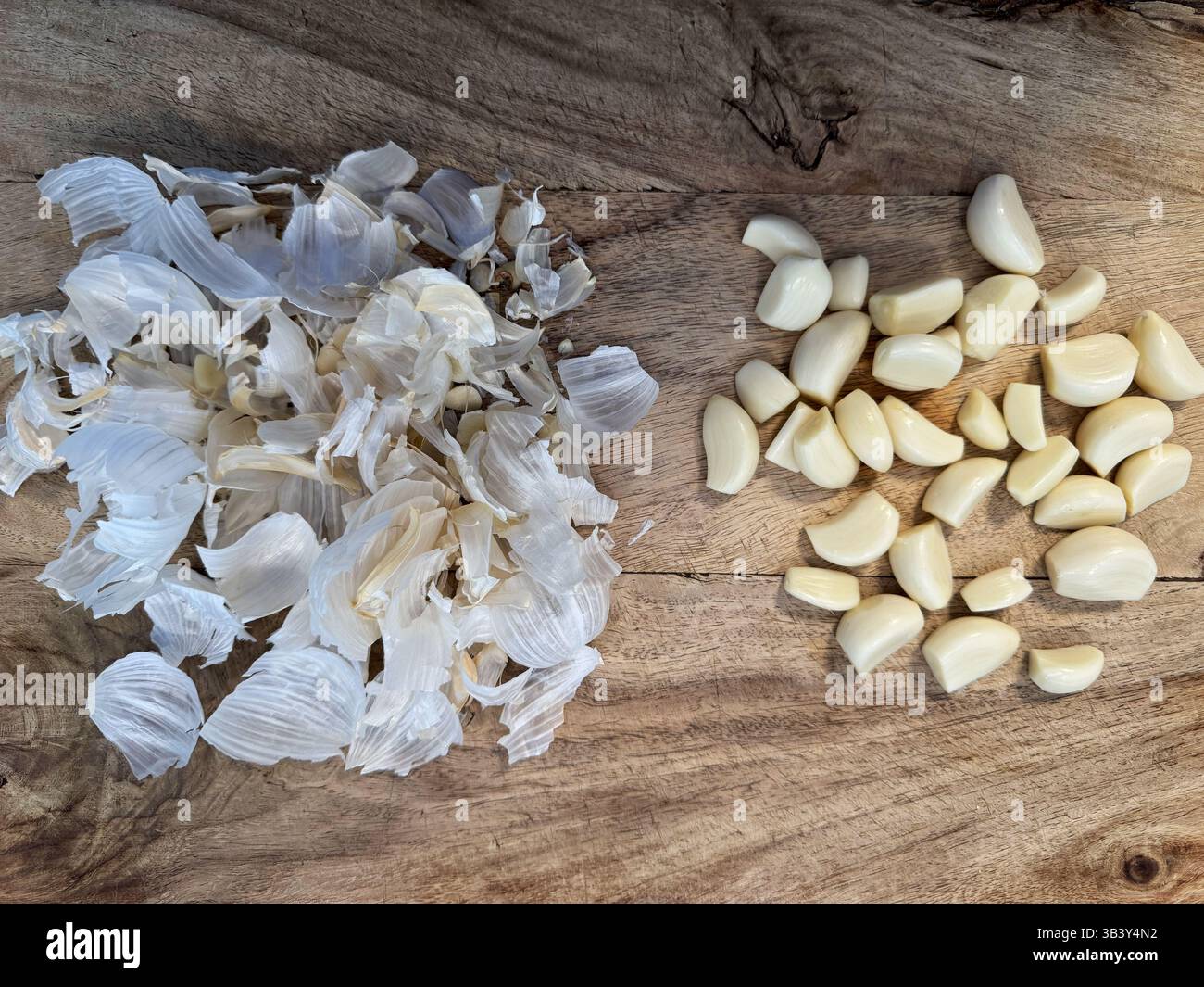 Peeled garlic cloves and papery garlic peels on a wooden cutting board - Smartphone Captured Stock Image
