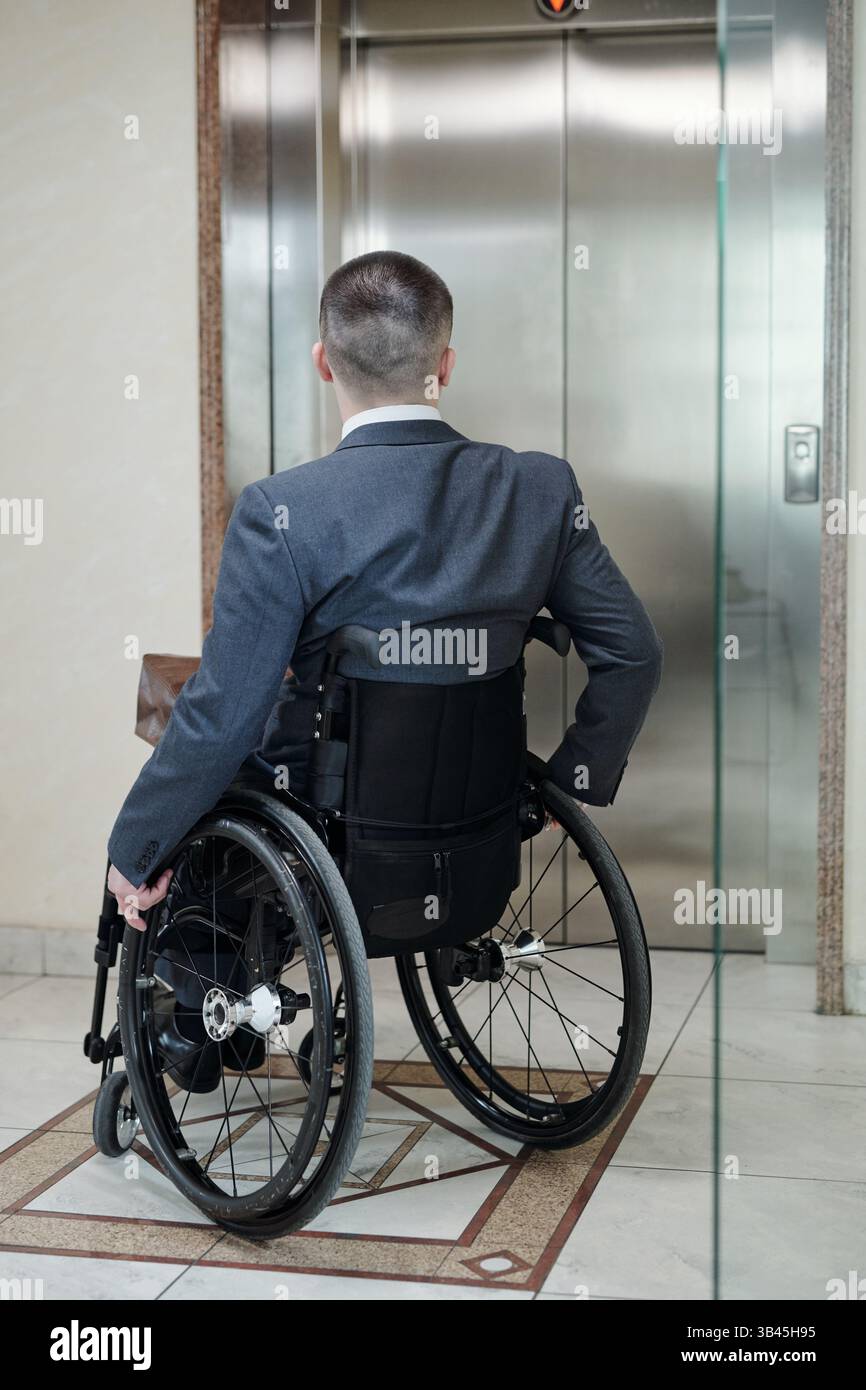 Disabled man in wheelchair waiting for elevator inside office building Stock Photo
