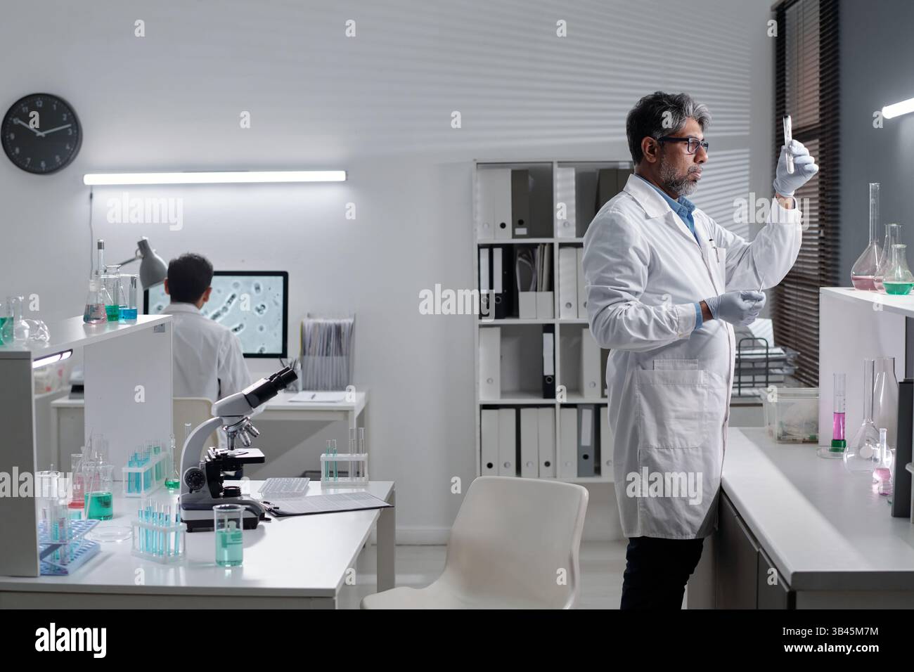 Researchers working in modern science lab, using microscopes and test tubes, analyzing samples and chemicals, surrounded by laboratory equipment and technology Stock Photo
