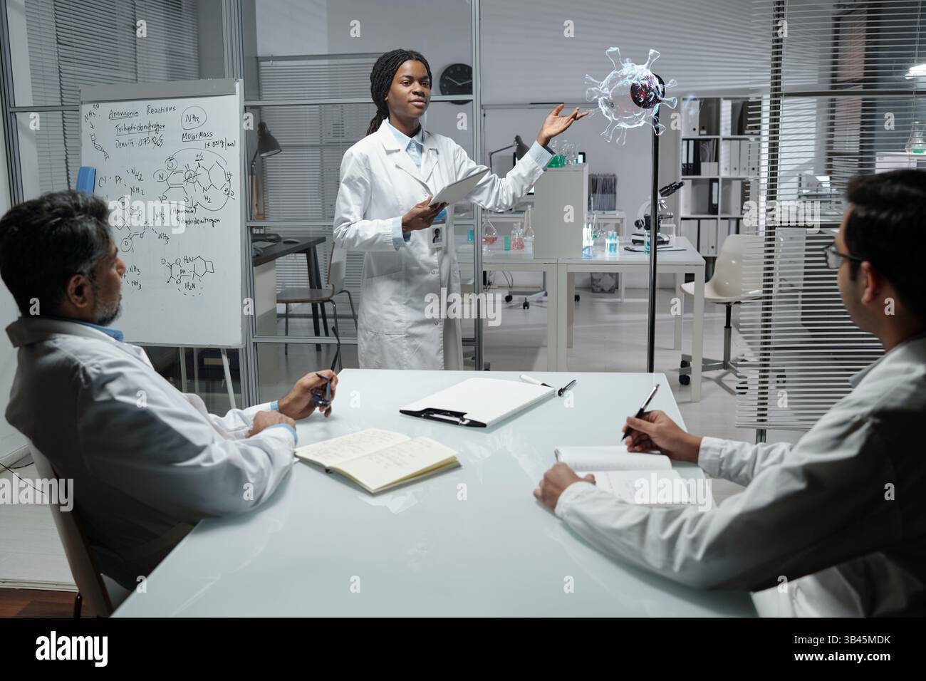 Scientist explaining complex molecular structures during presentation in laboratory setting with colleagues observing and taking notes Stock Photo