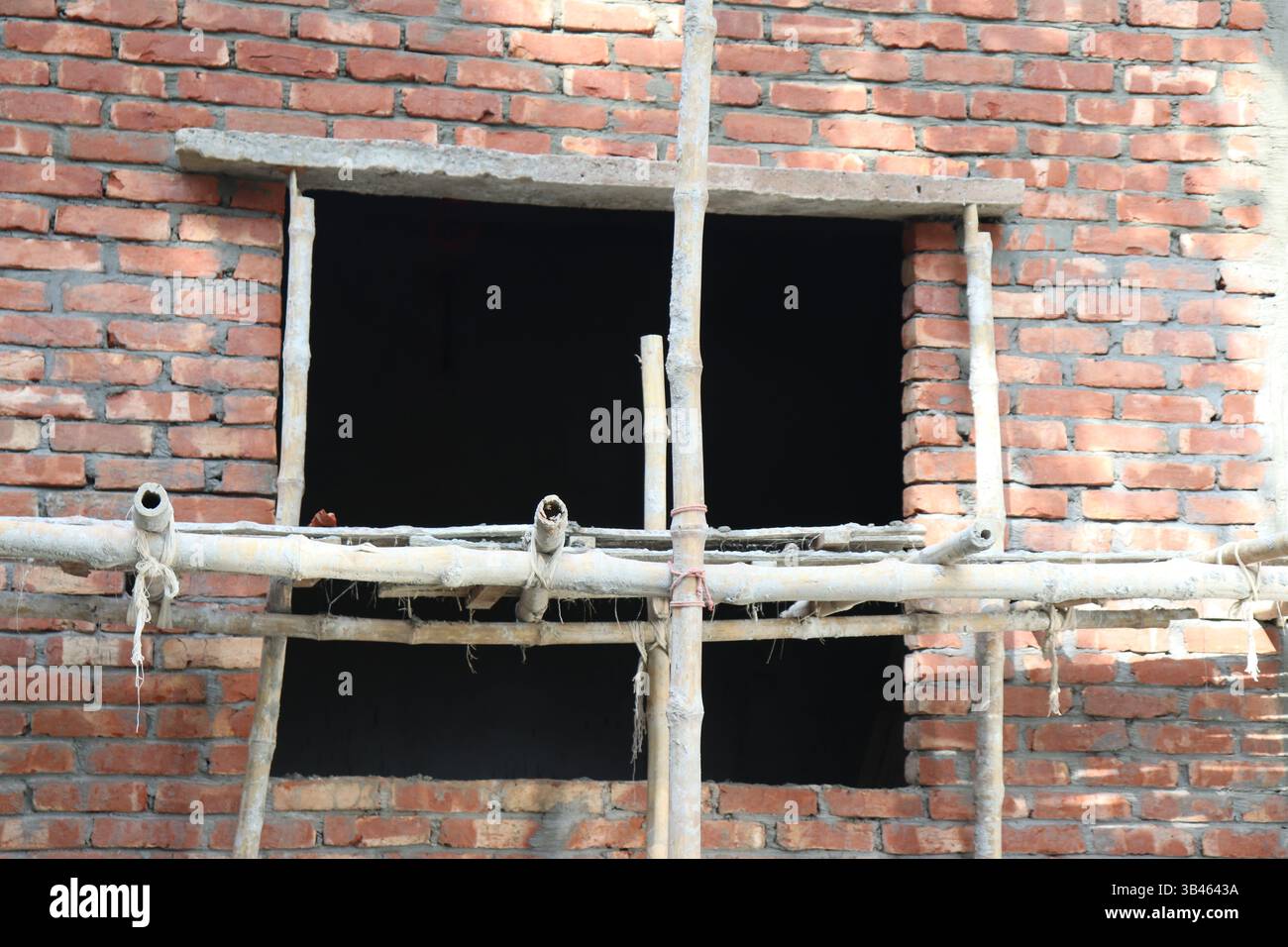 Construction of brick wall. Window opening showing black space. Bamboo ...