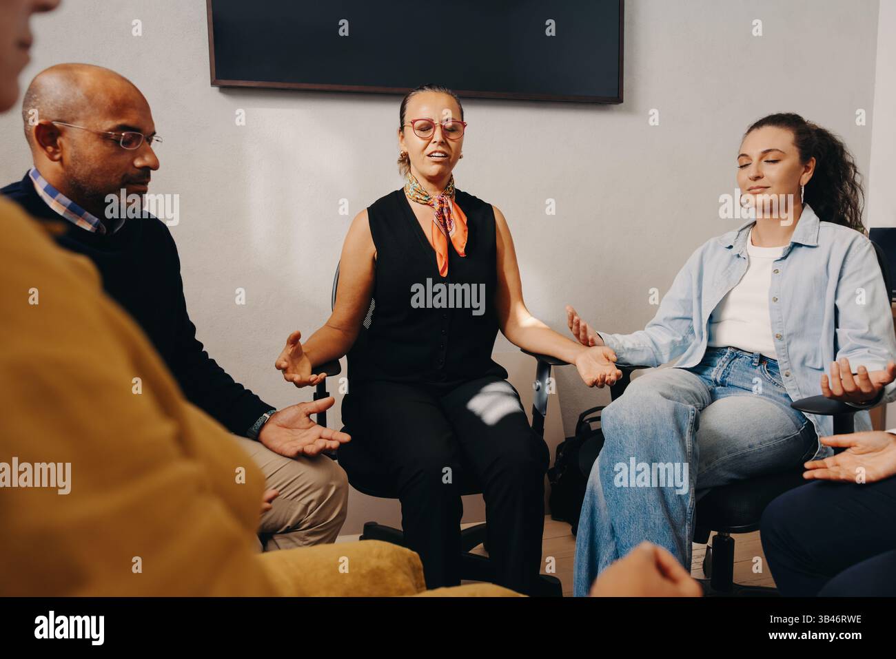 A diverse group of individuals engages in guided breathing exercises in a professional workspace, promoting mindfulness, relaxation, and teamwork for Stock Photo