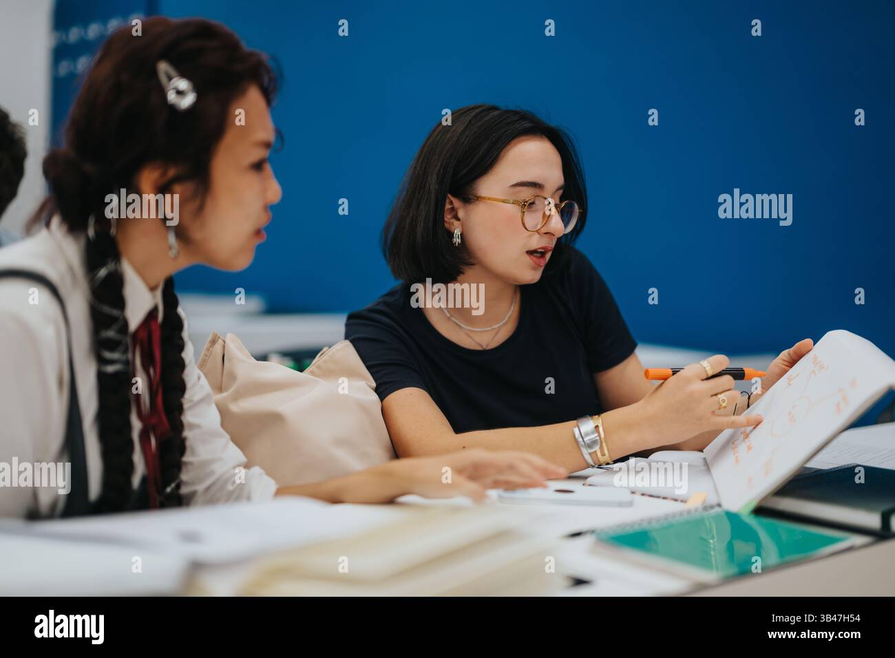 Students collaborating on class tasks with assistance from professor Stock Photo