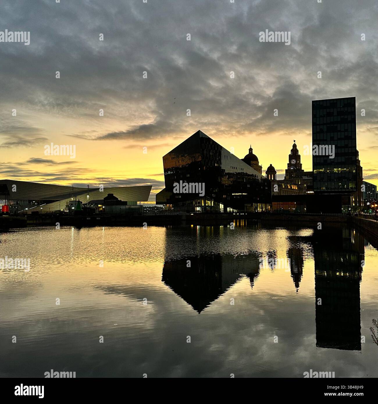Liverpool waterfront skyline with the Royal Liver Building and Museum of Liverpool reflected in calm evening water under a soft sunset sky. - Smartphone Captured Stock Image