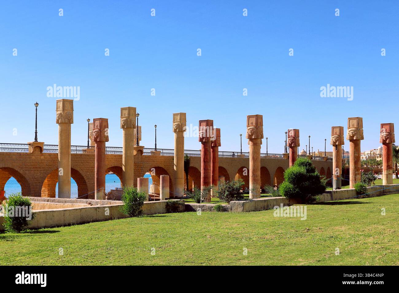 Decorative pharaonic-style columns with carved heads along the Sahl Hasheesh promenade, with stone arches, lanterns, and a view of the Red Sea. Stock Photo