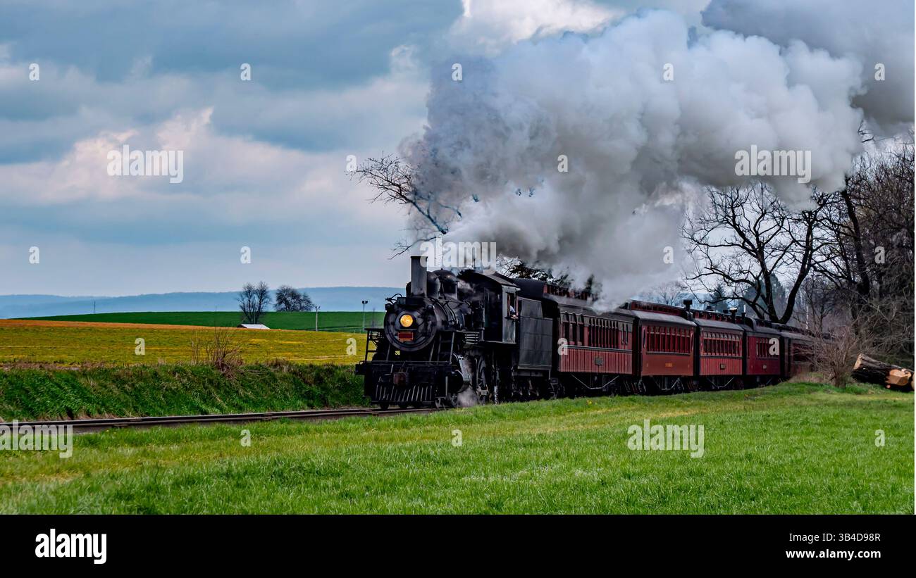 A steam locomotive chugs along the railway, releasing white smoke while ...