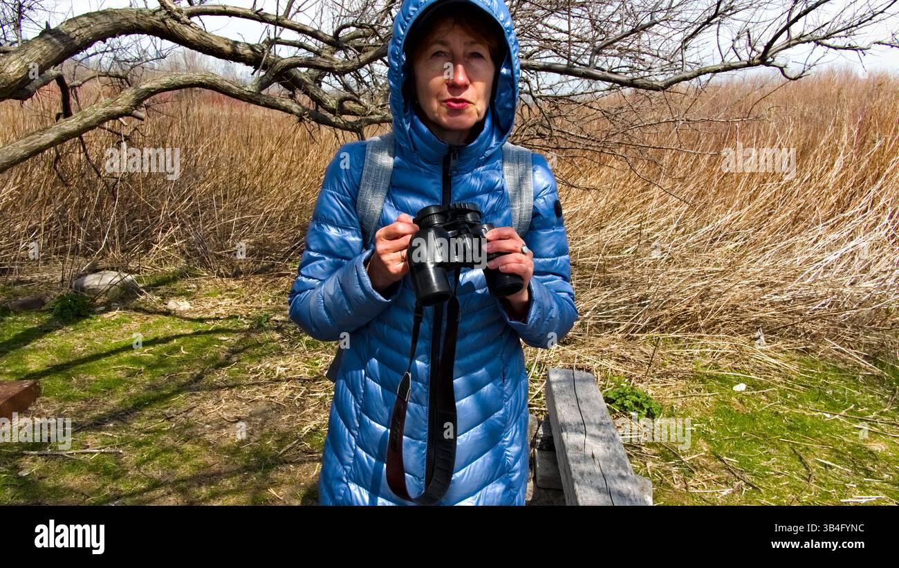 A woman wearing a blue jacket and cap scans the landscape with ...