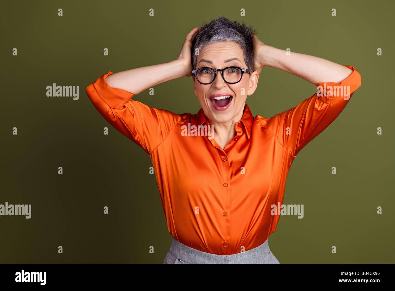 Smiling mature woman in orange shirt and glasses posing happily against ...