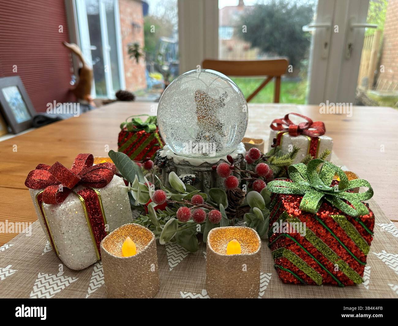 Close-up of Christmas table centrepiece with snow globe, berries and glittery presents, side view with soft festive lighting. - Smartphone Captured Stock Image