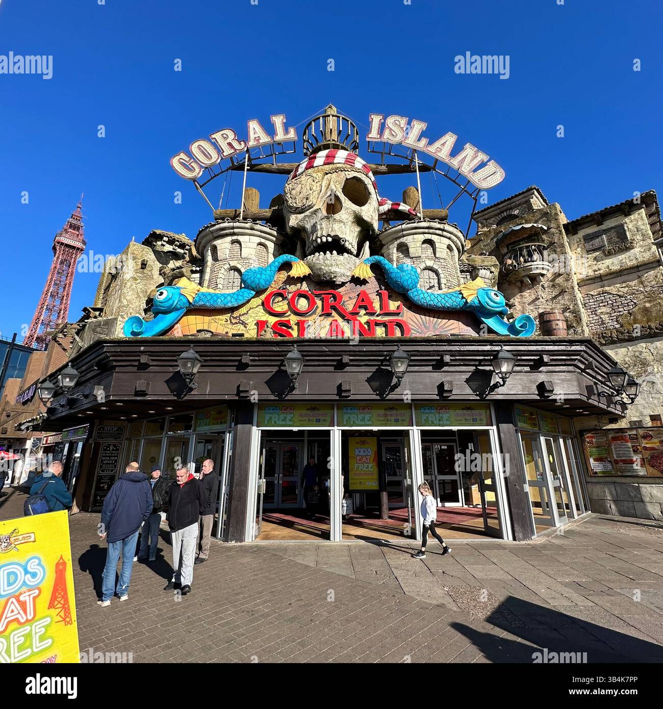 Coral Island amusement arcade in Blackpool on a bright sunny day with blue skies, with people walking past and into the iconic pirate-themed entrance. - Smartphone Captured Stock Image