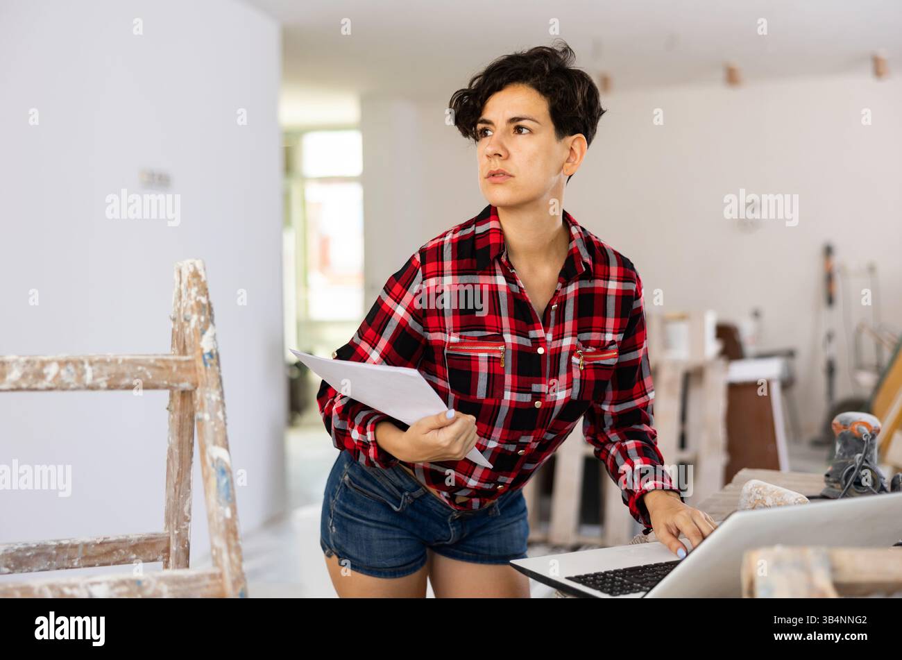 Woman builder checking project documentation and using laptop while working Stock Photo