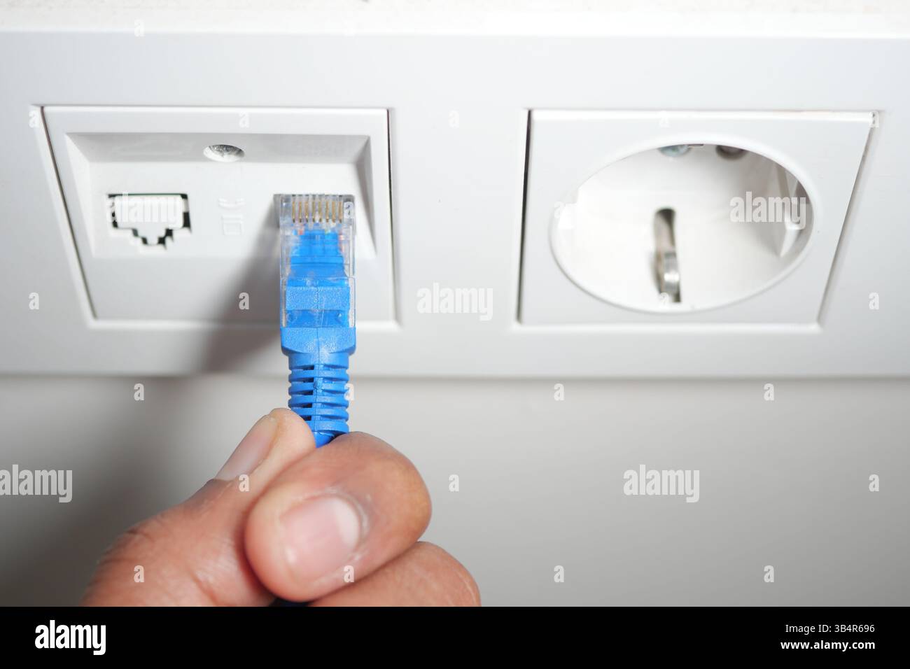 Connecting an ethernet cable to a wall socket in a modern setting Stock Photo