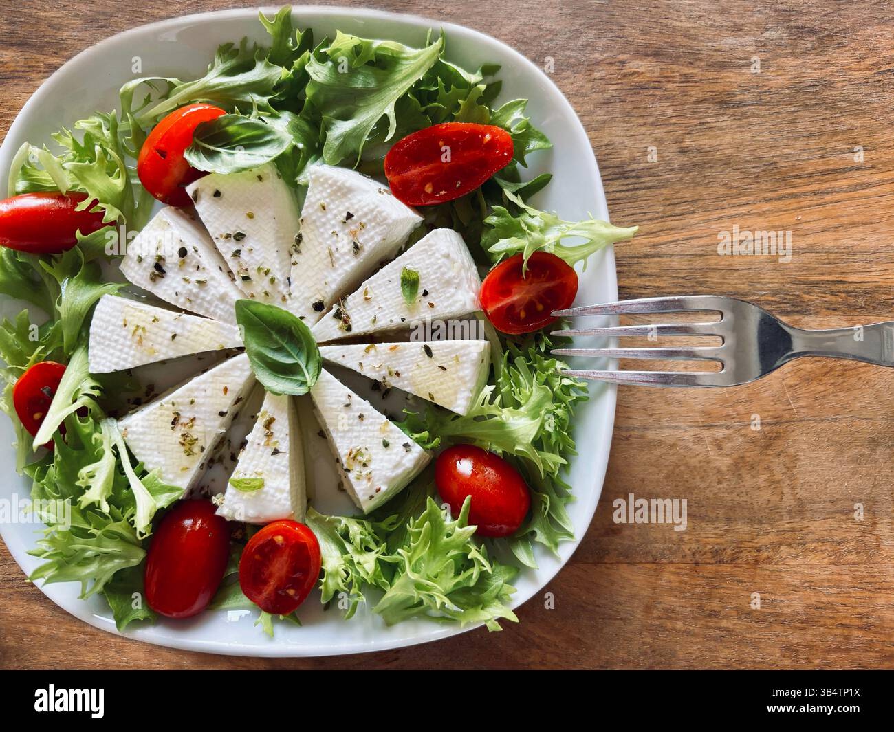 "Primosale", typical sicilian pecorino cheese. Fresh cheese with vegetables and basil leaf, olive oil on a white plate wooden background. Stock Photo