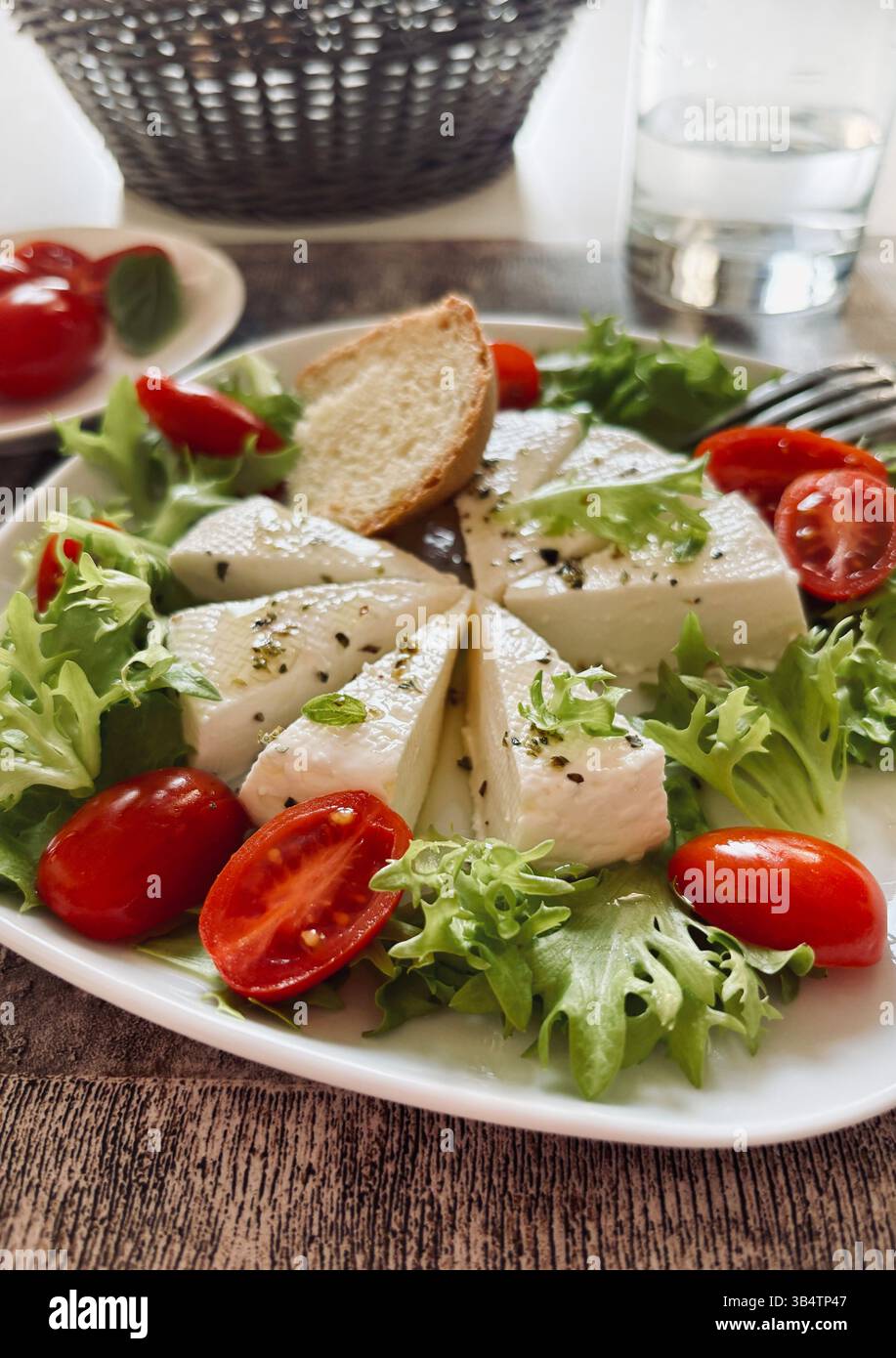 "Primosale", typical sicilian pecorino cheese. Fresh cheese with vegetables and basil leaf, olive oil on a white plate on the table. Stock Photo