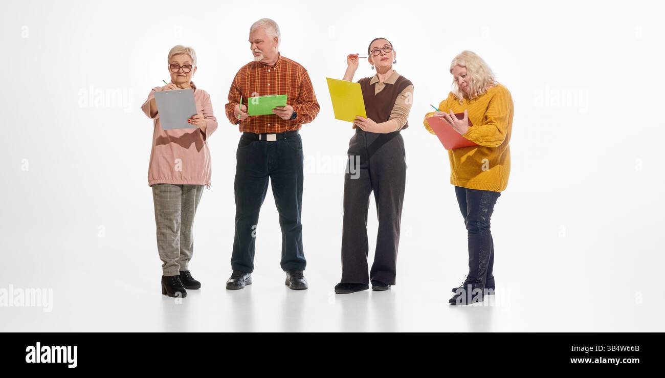 Group of senior students standing and writing, taking notes, on colorful clipboards against white studio background. Active minds in mature age. Stock Photo