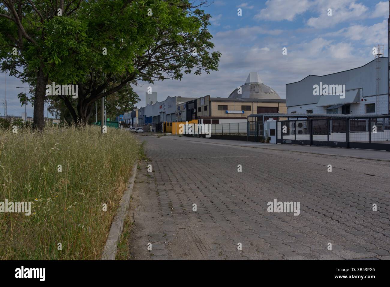 Paved road leading through an industrial estate with warehouses, factories, and storage facilities, suggesting economic activity and manufacturing Stock Photo