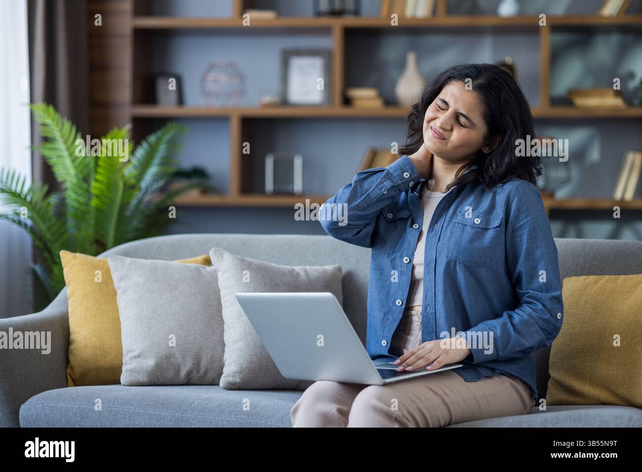 Tired young Indian woman sitting on sofa at home, massaging neck with ...