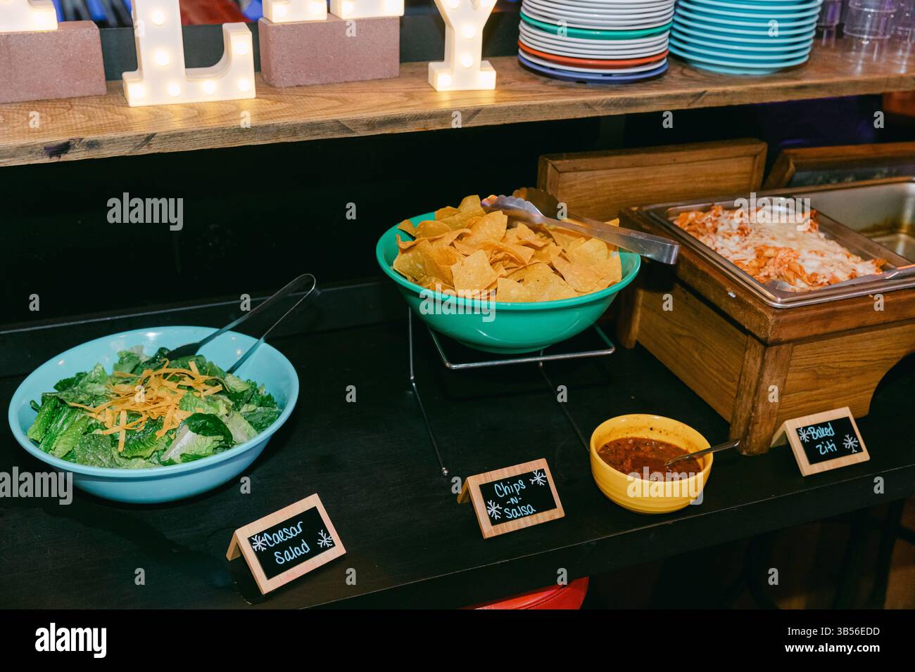 A vibrant buffet spread features fresh salad, crispy chips, and zesty salsas in an inviting event space. Stock Photo