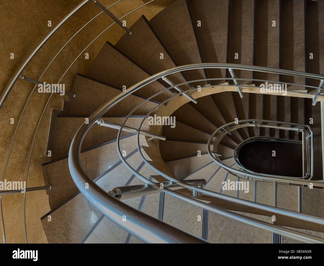 Top view of modern spiral staircase with metal railings and brown steps in public building interior. Geometric pattern,architectural detail,no people. - Smartphone Captured Stock Image