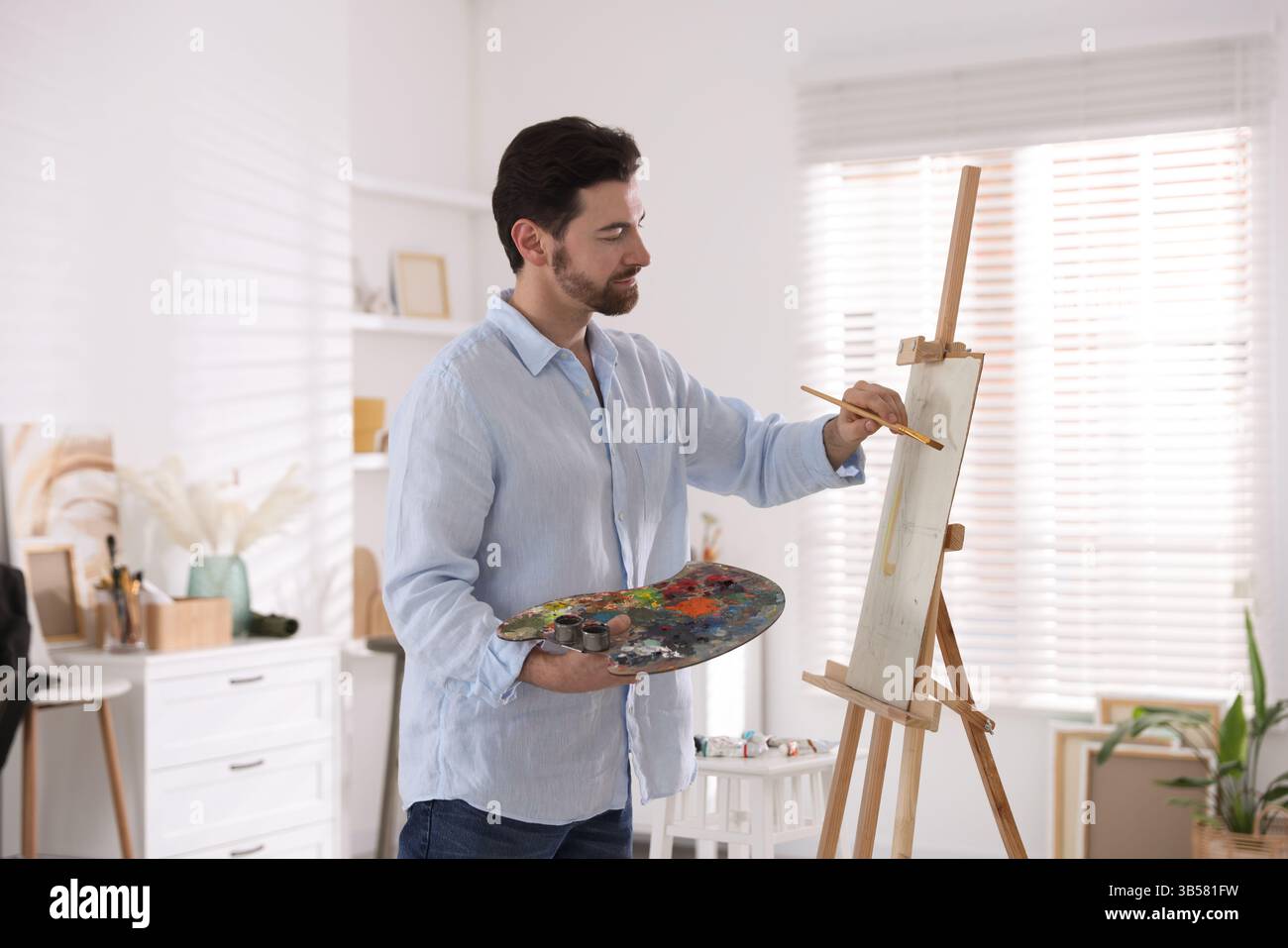 Man painting picture on easel in artist's studio Stock Photo - Alamy