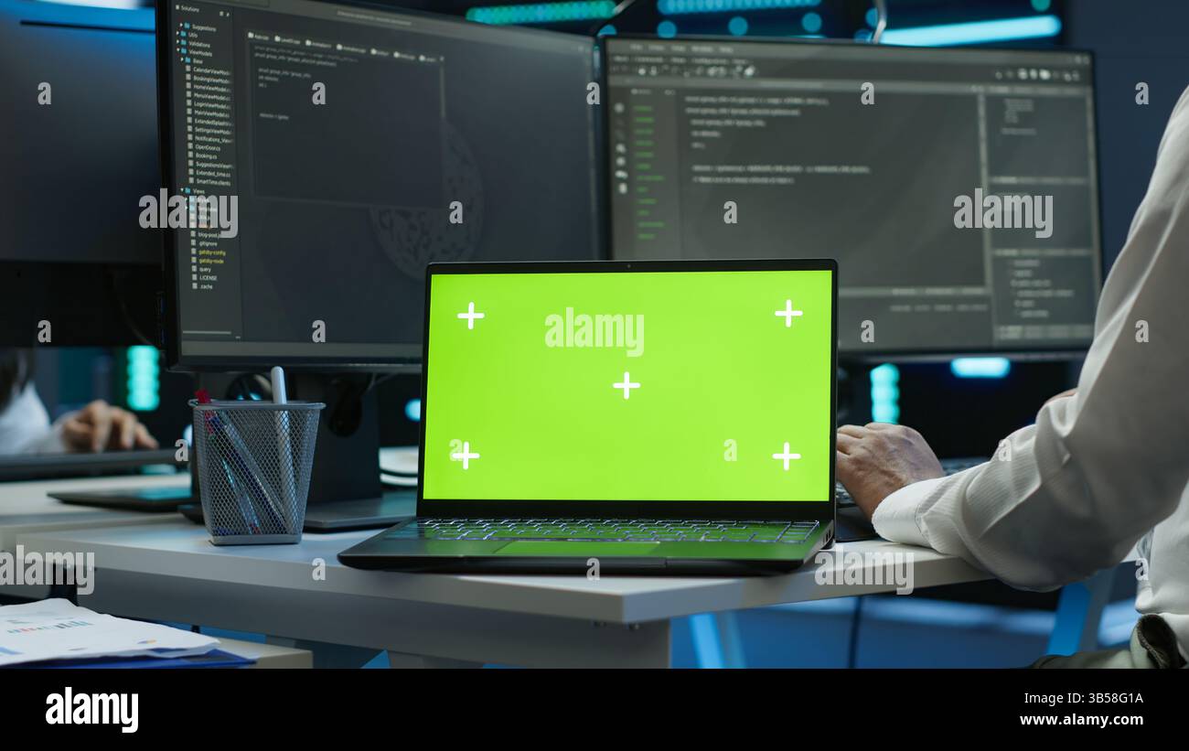 System administrator in data center installing software on isolated screen laptop, troubleshooting issues. Admin uses mockup notebook in server hub, establishing performance benchmarks, camera A Stock Photo
