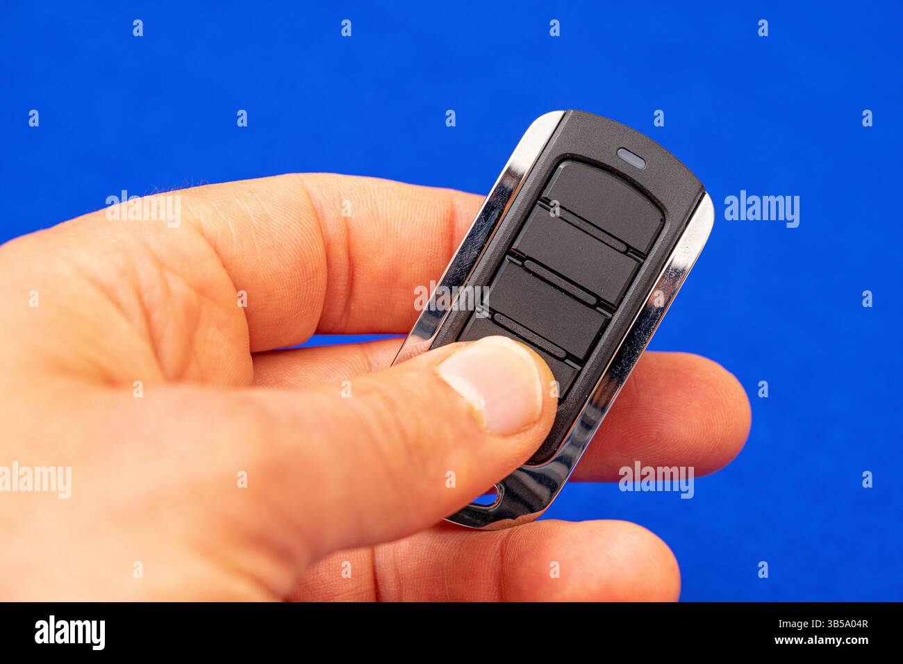 four-button remote control for opening garage doors held in hand on blue background Stock Photo