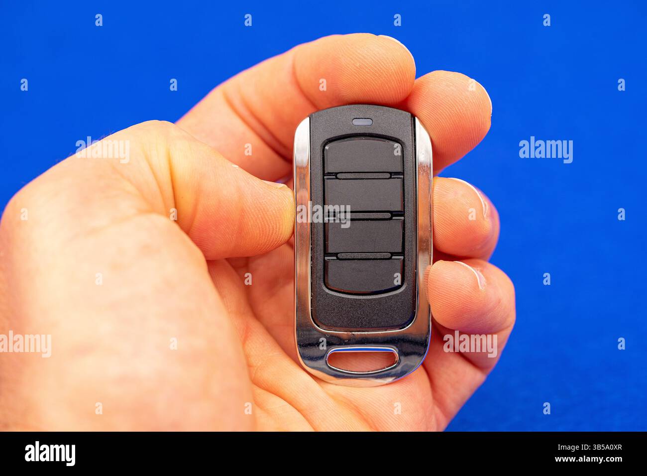 four-button remote control for opening garage doors held in hand on blue background Stock Photo