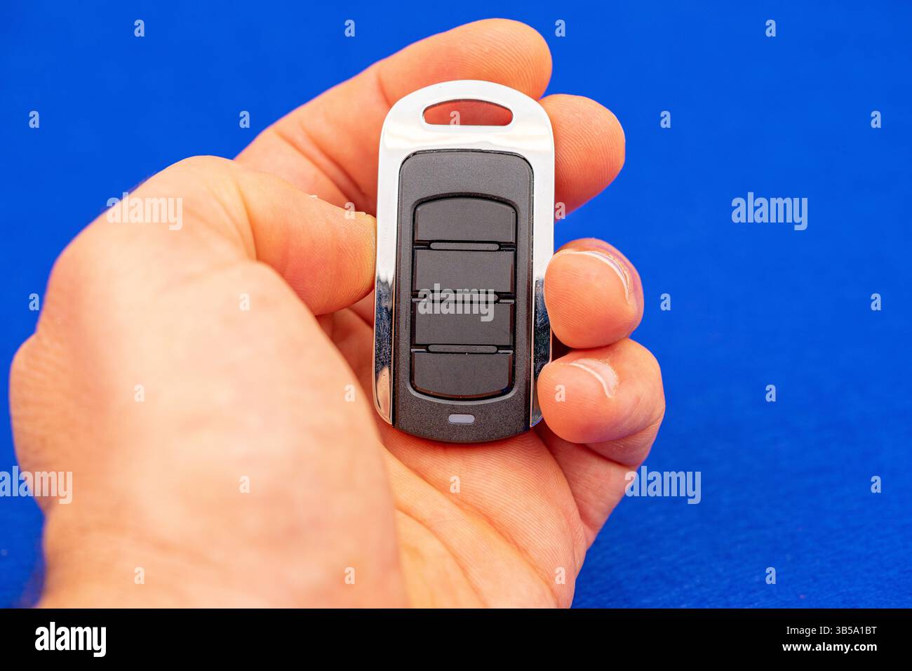 four-button remote control for opening garage doors held in hand on blue background Stock Photo
