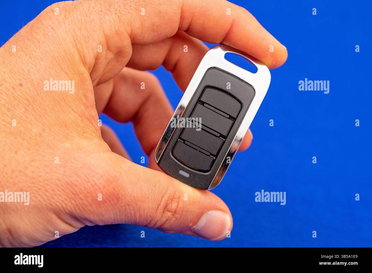 four-button remote control for opening garage doors held in hand on blue background Stock Photo
