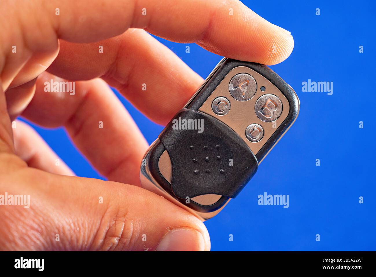 four-button remote control for opening garage doors held in hand on blue background Stock Photo