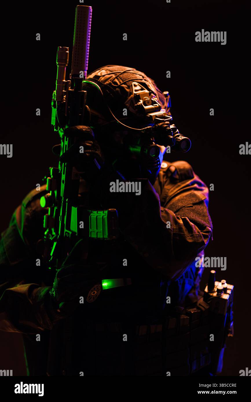 A tactical operative holding a firearm equipped with night vision gear and illuminated by cinematic green and blue lights, embodying a stealthy and pr Stock Photo