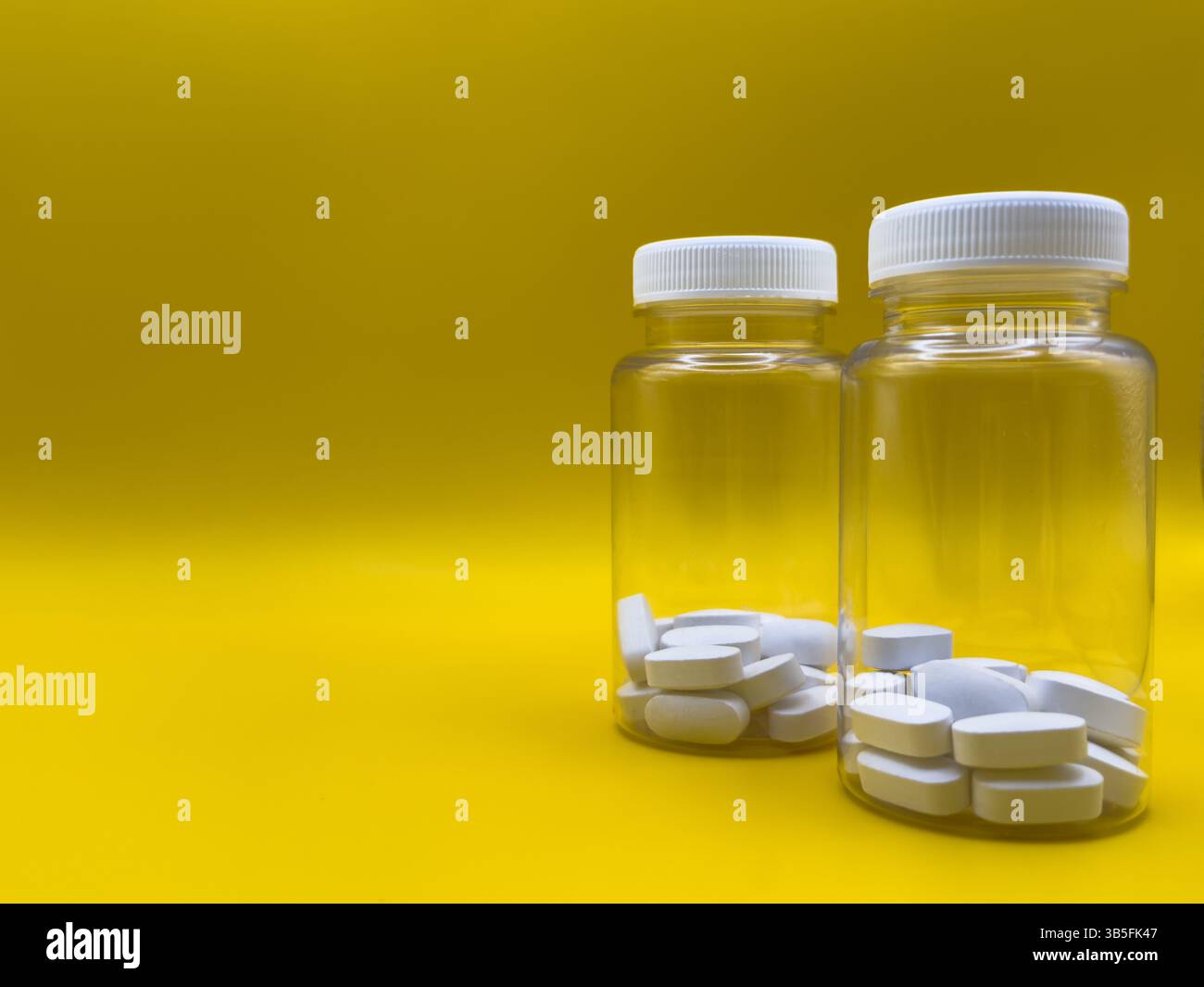 White tablets in two transparent jars on yellow background, front view, against virus and cold Stock Photo