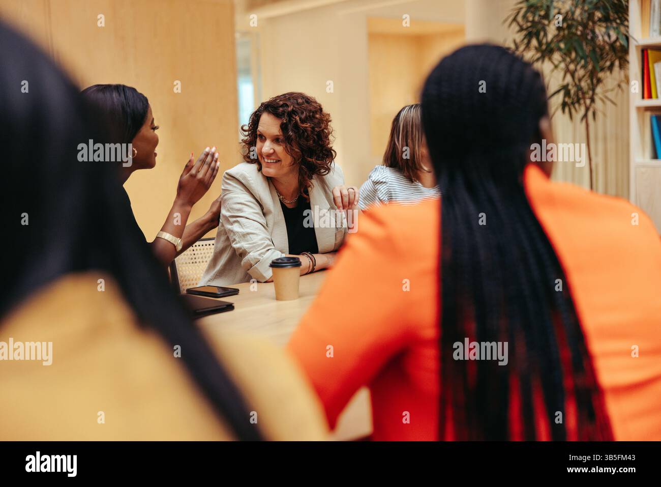 A group of female coworkers are seen discussing ideas around a conference table. The lively interaction captures teamwork, communication, and collabor Stock Photo