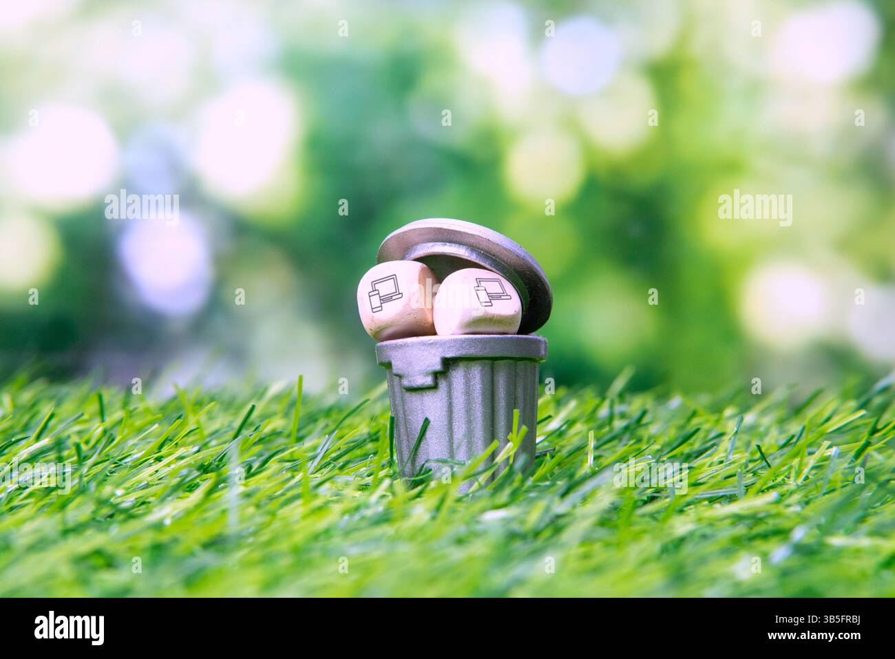 Trash can and two small wooden cubes with laptop and smartphone icon. Concept of electronic waste or e-waste disposal. Stock Photo
