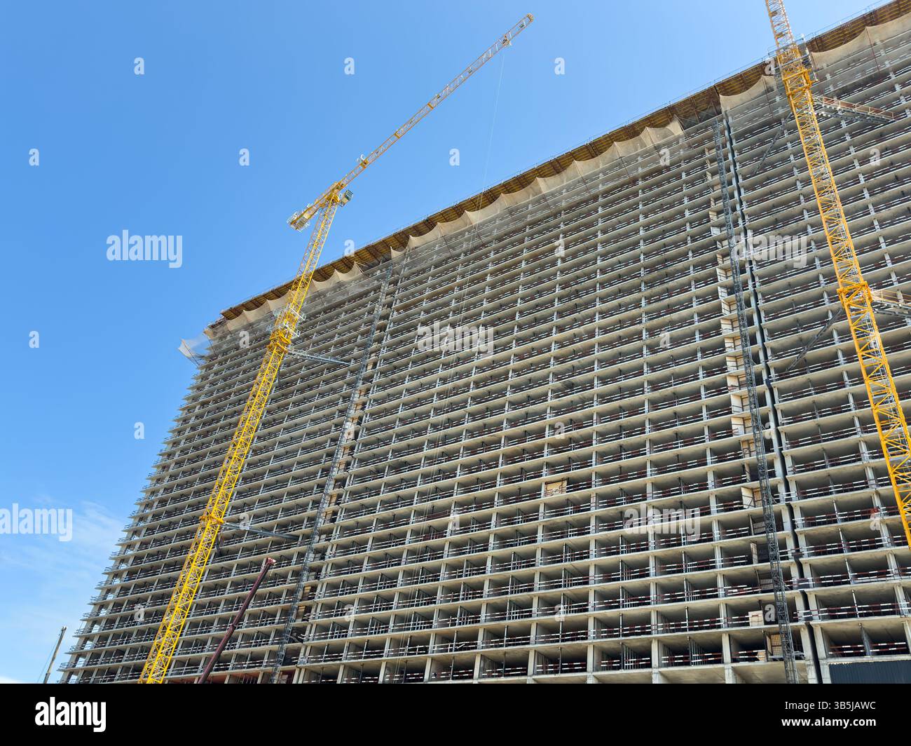 High-rise building under construction with concrete floors and tower cranes against clear blue sky.Urban development,architectural structure,no people - Smartphone Captured Stock Image